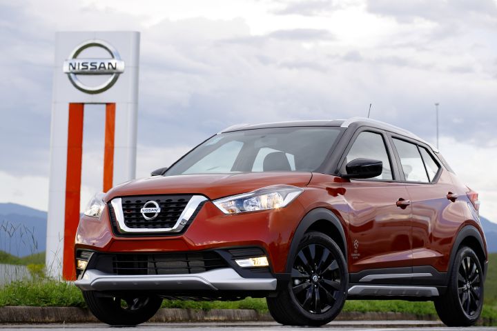 Kicks UEFA vermelho de ¾ de frente ao lado do totem da fábrica da Nissan