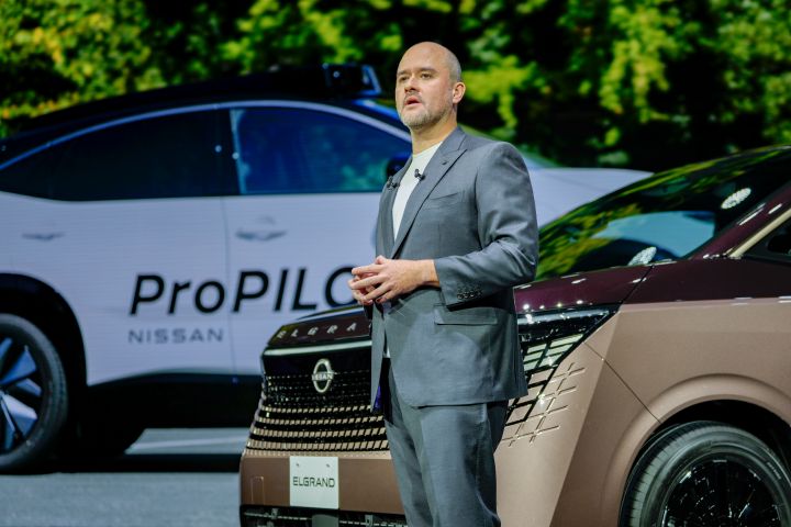 On the stage, the all-new Elgrand in Fuji Dawn and Shigoku two-tone colors is positioned diagonally, facing slightly to the left. Next to the vehicle stands Nissan CEO Ivan Espinosa in a suit, with hands clasped in front.