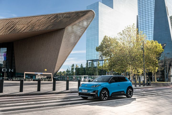 Ein blauer Nissan Micra parkt in der Sonne vor imposanter Architektur rund um den Hauptbahnhof von Rotterdam