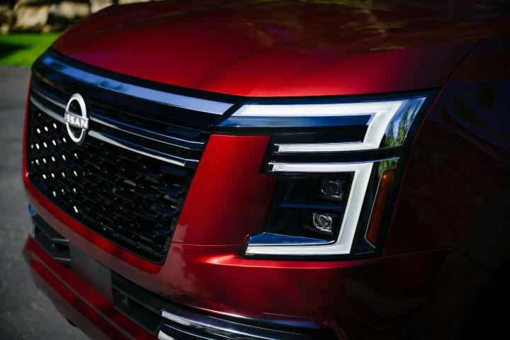 Angled close up of the front end on a red 2025 Nissan Armada, the headlights are on.