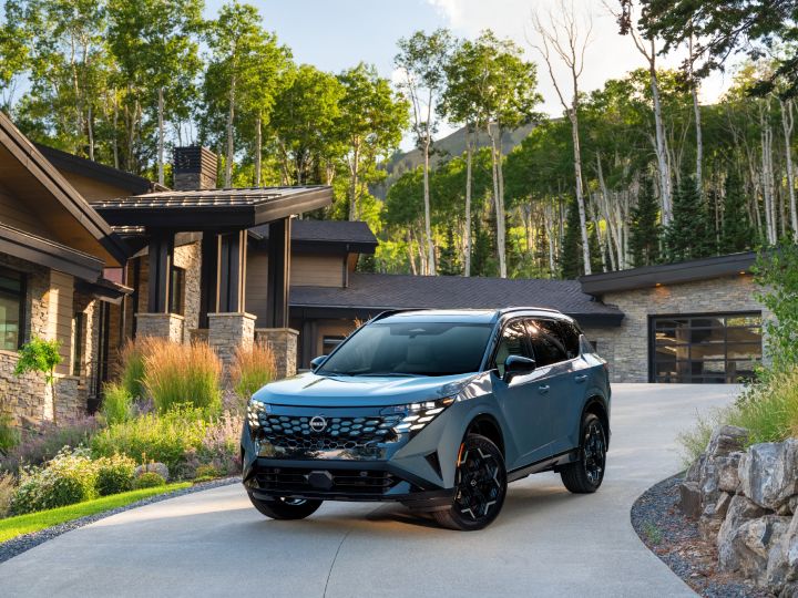 Front left 3/4 angle of the 2027 Nissan Rogue Hybrid Platinum parked in front of a house with trees behind.