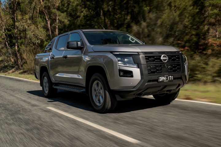 2026 Nissan Navara ST dual cab ute finished in Summit Silver photographed in motion from the front three-quarter view, highlighting the grille, wheels and side steps.