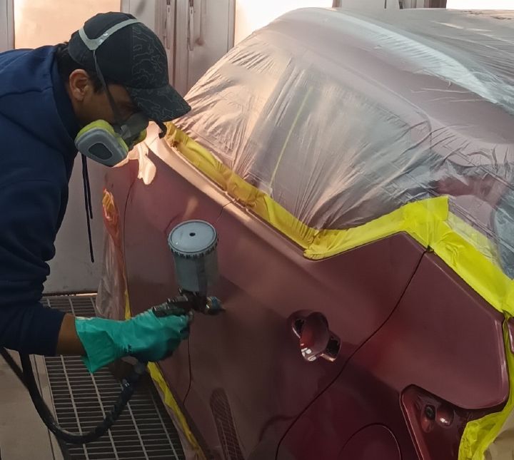 Hombre con mascarilla pintando vehículo Nissan rojo