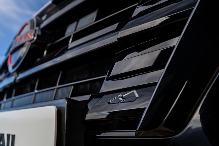 Nahaufnahme des neuen 2026 Nissan X‑Trail mit N-Trek-Kühlergrill und kleinem silbernen Emblem, das einen stilisierten Mount Fuji zeigt. Das Bild hebt das schlanke, glänzende Design und die modernen Details der Fahrzeugfront hervor.