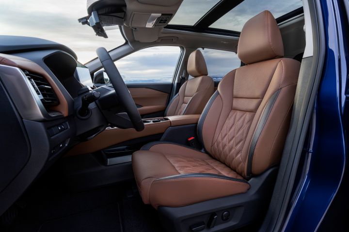 Der Innenraum des neuen 2026 Nissan X‑Trail konzentriert sich auf die Vordersitze und das Armaturenbrett und besticht durch kastanienbraune Premium-Stepplederpolster mit Rautensteppung und ein Panorama-Schiebedach. Zur Ausstattung gehören ein modernes Lenkrad, ein digitales Display und eine blaue Außenfarbe, die durch die geöffnete Tür sichtbar ist.