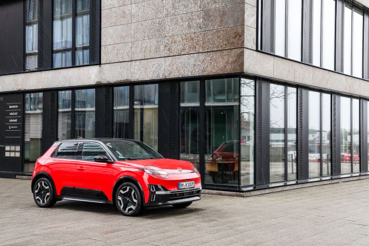 Blick von schräg vorne auf einen roten Nissan Micra, der vor einem Bürogebäude mit einer Fassade aus Glas und schwarzen Trägern steht