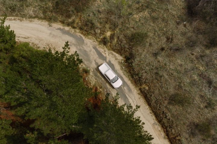 An arial shot of an Alpine White 2026 Nissan Navara driving on a bend in a dirt road.