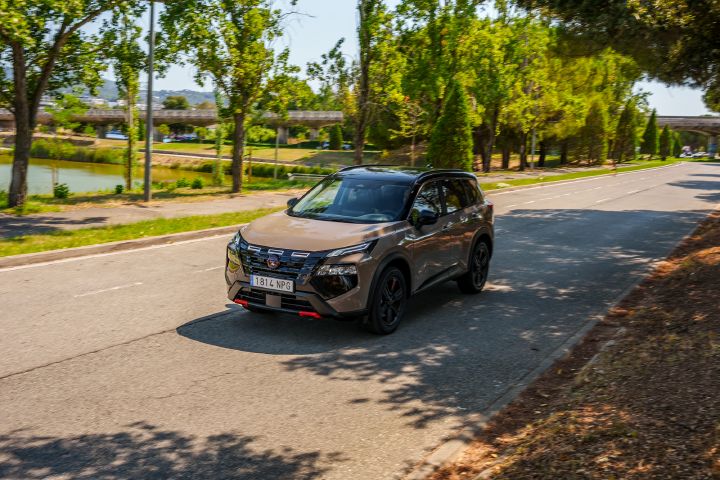Dreiviertelansicht von schräg oben auf den Nissan X‑Trail. Im Hintergrund sind Bäume und eine Brücke zu sehen