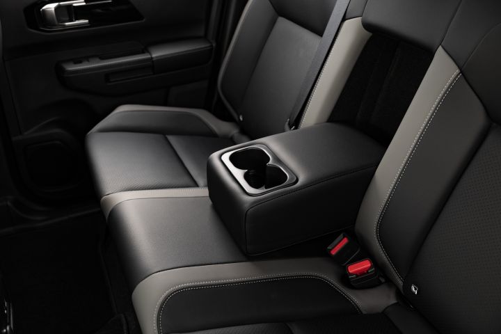 Close-up of the rear seat in a 2026 Nissan Navara ST‑X with the fold-down centre armrest lowered, showing two integrated cupholders, contrast stitching, and the rear door trim.