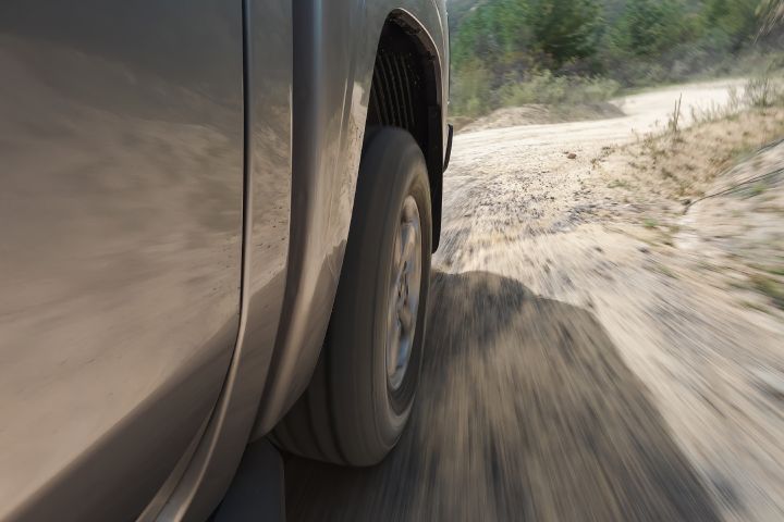 2026 Nissan Navara ST dual cab ute finished in Summit Silver shown in a close moving view of the rear wheel on a sandy track.