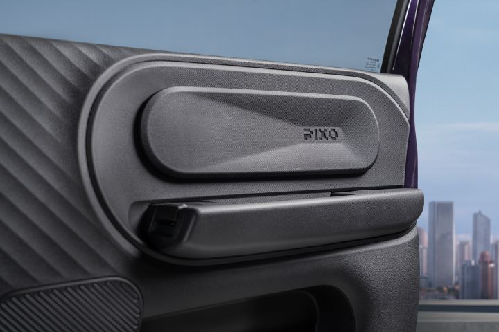 Close-up photograph of a vehicle door panel featuring quilted upholstery, metallic trim, speaker grille, and embossed “PIXO” branding. Open door frames a modern city skyline, highlighting refined interior design.