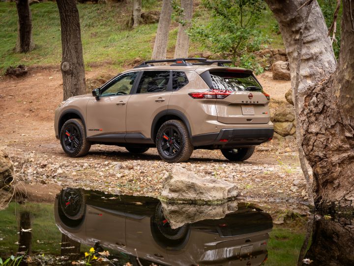 Left rear 3/4 view of a 2025 Nissan Rogue rock creek parked along a wooded creek that is reflecting its image.