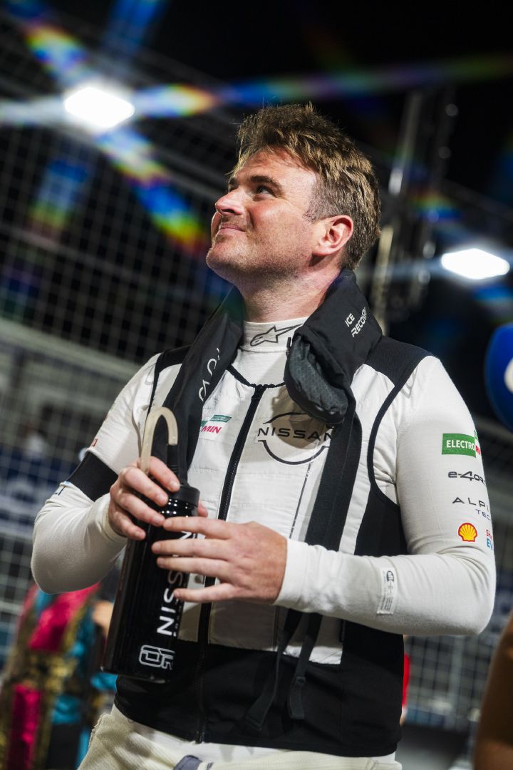 Porträtfoto von Oliver Rowland, der vor dem E-Prix in Tokio mit seiner weißen Kühlweste in der Startaufstellung steht und lächelnd nach oben sieht.