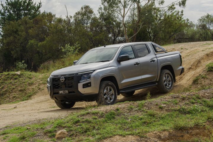 2026 Nissan Navara ST dual cab ute finished in Summit Silver shown from the front three-quarter angle on uneven off-road terrain.