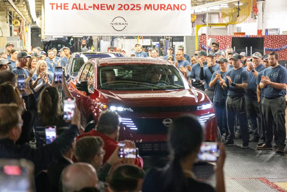 A red 2025 Nissan Murano slowly driving between crowds of Nissan workers.