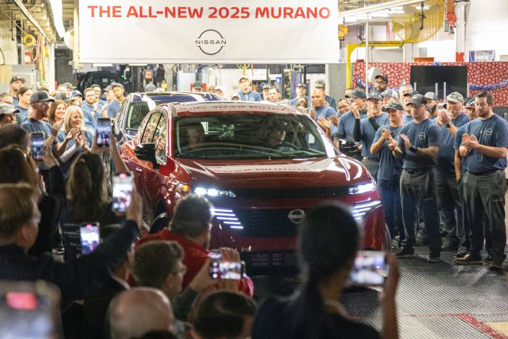 A red 2025 Nissan Murano slowly driving between crowds of Nissan workers.