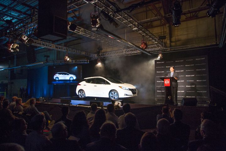 A man presenting the  2018 Nissan LEAF at an automotive event with an audience and stage lighting.