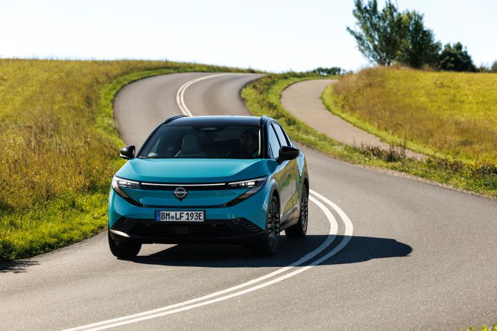 Auf einer kurvigen Landstraße mit gelbgrünen Feldern zu beiden Seiten fährt ein türkiser Nissan LEAF