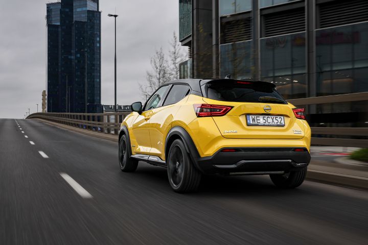 Jadący żółty Nissan Juke (widok z tyłu) z budynkami w tle