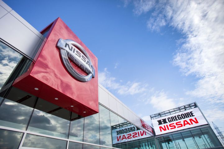 L'extérieur d'une concession Nissan avec de grands logos Nissan sur le bâtiment sous un ciel partiellement nuageux.