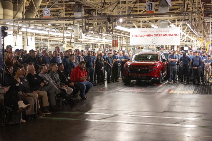 A red 2025 Nissan Murano parked near a large crowd of Nissan workers.