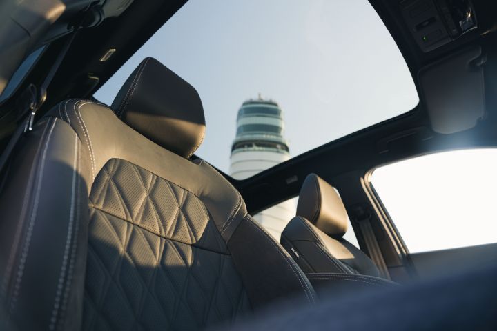 Blick aus dem Panorama-Glasdach von den Vordersitzen im Innenraum des Nissan Qashqai auf einen weißen Turm