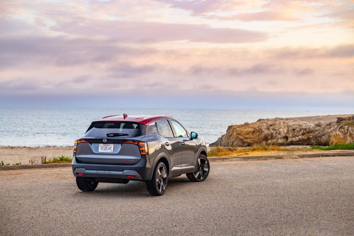 Right rear 3/4 view of a silver 2025 Nissan Kicks parked on a gravel lot overlooking the ocean during sunset.