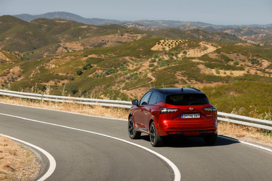 Nieuwe Nissan Qashqai in de kleur Fuji Sunset Red, van de achterzijde gezien, rijdend op een  weg in Portugal