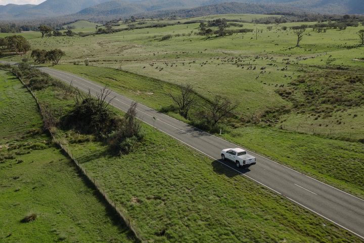 2026 Nissan Navara SL dual cab ute finished in Alpine White viewed from a high aerial angle on a straight country road beside open paddocks.