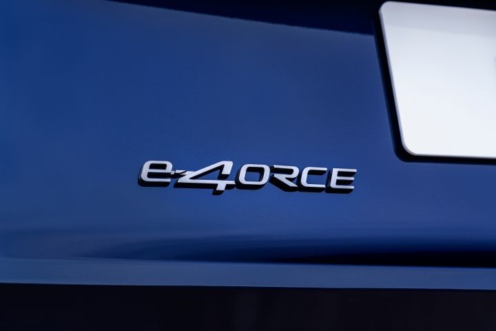 Nissan X‑Trail Tekna in der Karosseriefarbe Universal Blue mit Nahaufnahme eines metallischen „e‑4ORCE”-Emblems auf glänzendem Blau auf der Rückseite. Die Allradsteuerung e‑4ORCE bietet außergewöhnliche Bodenhaftung, Stabilität, Sicherheit und Komfort unter verschiedenen Straßenbedingungen.