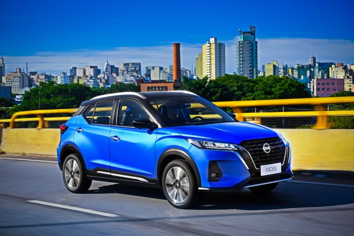 Nissan Kicks azul roda por viaduto amarelo com paisagem de prédios ao fundo.
