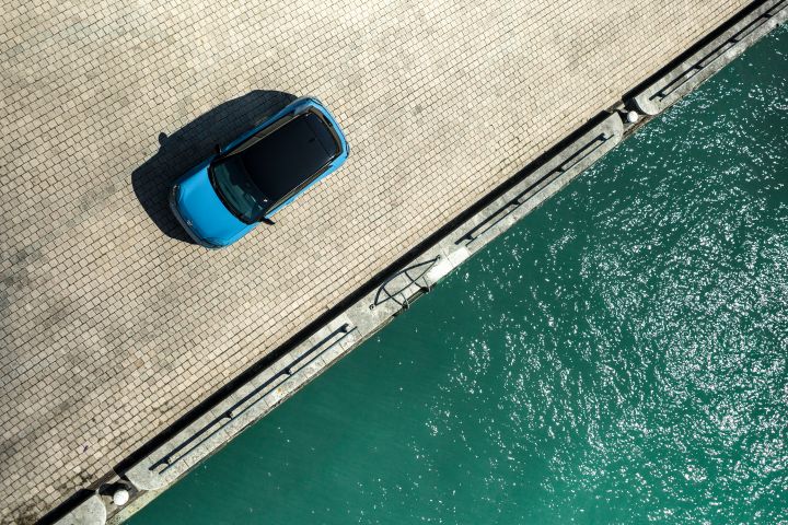 Zweigeteiltes Bild aus der Vogelperspektive, links steht ein Micra auf einem gepflasterten Platz, rechts ist türkises Wasser zu sehen