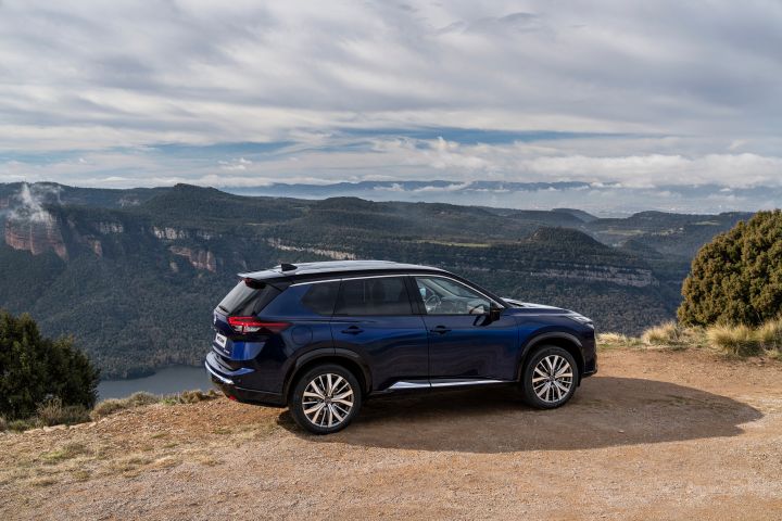 Neuer 2026 Nissan X‑Trail Tekna in der Außenfarbe Universal Blue, geparkt auf einem unbefestigten Aussichtspunkt mit weitläufiger Berglandschaft und bewölktem Himmel im Hintergrund. Die Szene unterstreicht das schnittige Design und die robuste Leistungsfähigkeit des Fahrzeugs, das sich ideal für Outdoor-Abenteuer eignet.