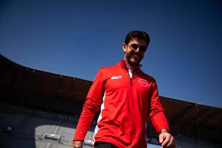 Norman Nato lächelt, während er sein Nissan Formula E Team-Sweatshirt und seine Sonnenbrille trägt und auf der Rennstrecke in Mexiko-Stadt spazieren geht.