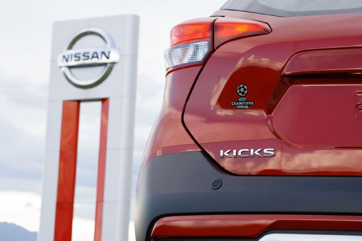 Detalhe da traseira do Kicks UEFA vermelho do lado esquerdo com o totem da fábrica da Nissan ao fundo