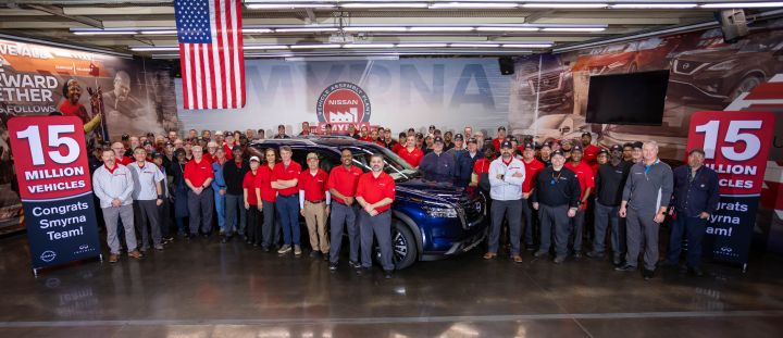 A large crowd of employees standing by a Nissan car and red banners and signs that read 15 Million Vehicles.