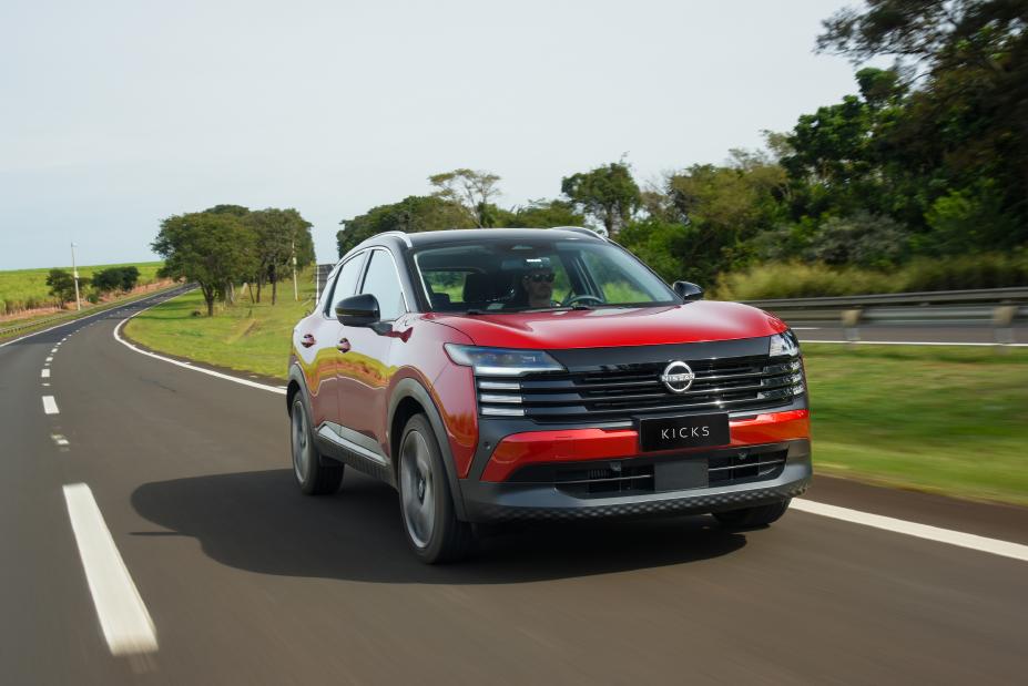Novo Nissan Kicks vermelho em movimento em uma rodovia. Ao lado direito, um fundo com árvores