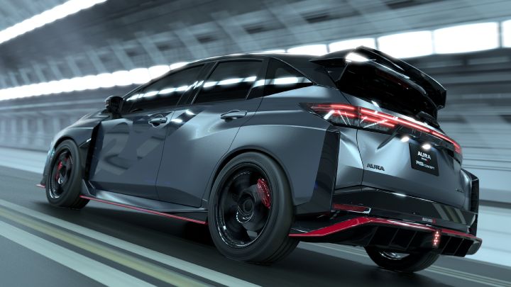 A silver and black two-tone sports car, the Aura Nismo RS Concept, speeding through a tunnel in a rear-right angled view. The vehicle features a large rear wing, with a black plate displaying white text reading 'AURA NISMO RS CONCEPT' at the center of the rear, along with a red accent line and the 'NISMO' logo on the lower bumper. The black wheels with red brake calipers stand out, while the blurred tunnel walls in the background emphasize motion and dynamic speed