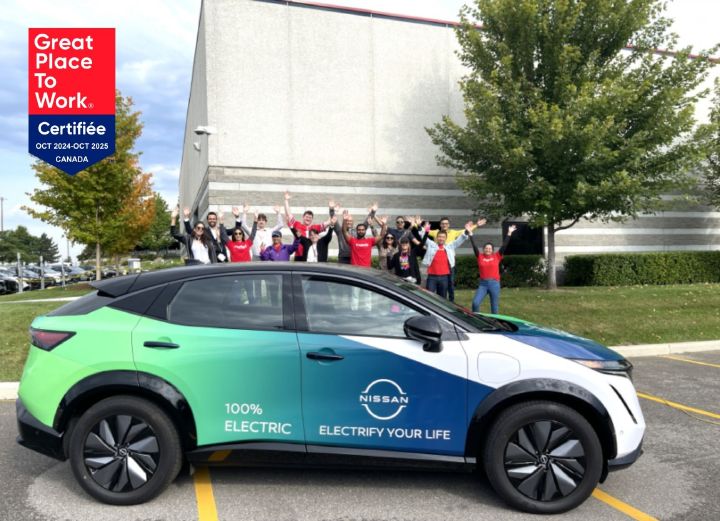 Un grand groupe d’employés de Nissan posant pour une photo de groupe devant un Nissan Ariya 2024 emballé et un bâtiment de l’entreprise en arrière-plan