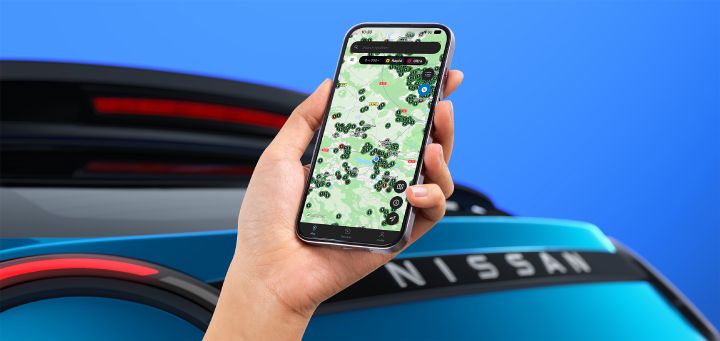 Eiine Hand hält vor dem Heck eines Nissan Micra ein Smartphone, auf dem die Nissan Charge App zu sehen ist. Die App-Ansicht zeigt, wie Kunden einfach und gefiltert nach Ladestationen für Elektrofahrzeuge suchen können.