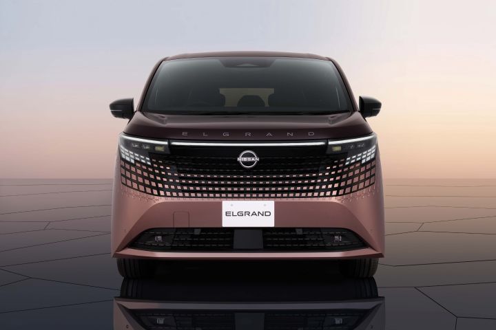 A Fuji-dawn-colored Elgrand is photographed from the rear, with the “NISSAN” and “ELGRAND” license plates visible. The rear design is emphasized, set in an outdoor exhibition space.