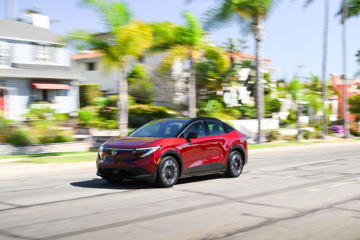 Front left 3/4 view of the 2026 Nissan LEAF driving along a palm tree-lined residential road.