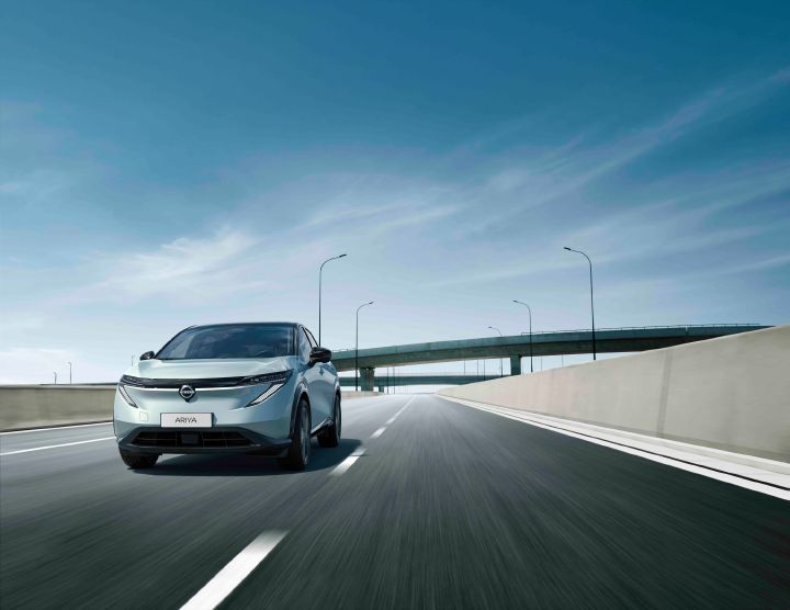 2027 Nissan ARIYA driving along a road line a highway bridge behind