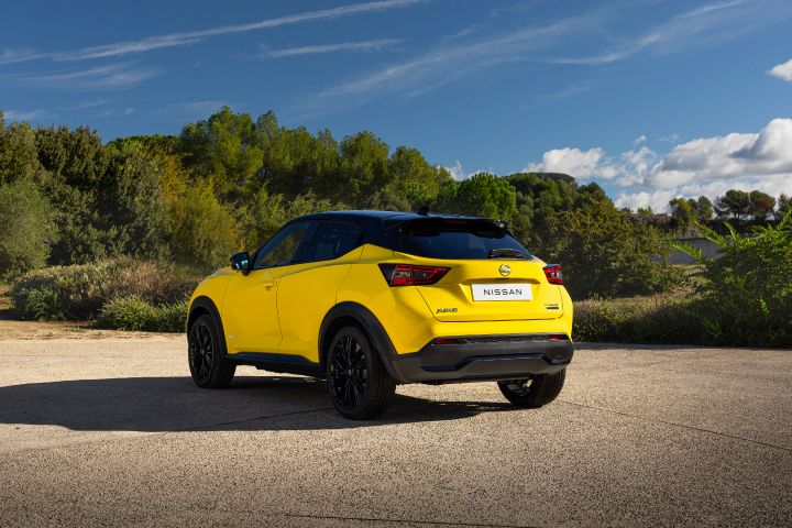 Gele Nissan Juke van achteren gezien, geparkeerd op de weg onder een blauwe hemel en met groene bomen op de achtergrond.