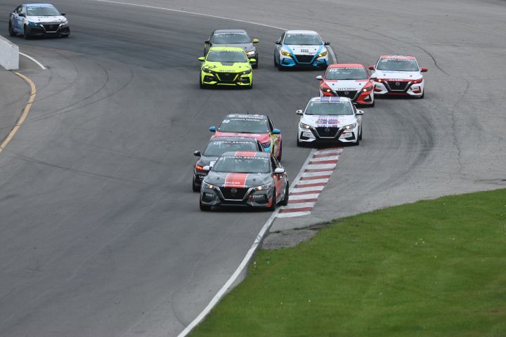 Multiple Nissan Sentra Racecars driving around the bend of a race track with a patch of grass on the bottom right