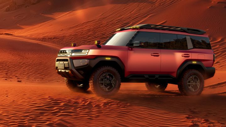 A red Terrano PHEV Concept parking to the left across desert dunes at sunset. Rolling sand and rocky terrain extend into the background, illuminated by warm evening light.
