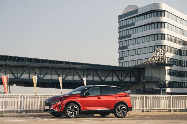 7/8 Frontansicht eines parkenden Nissan Qashqai in Fuji Sunset Red vor Flughafengebäuden