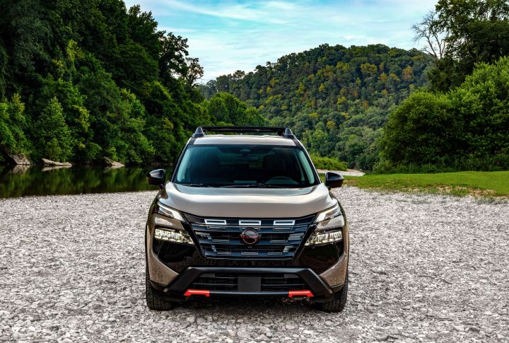 Front view of the 2025 Nissan rogue rock creek parked on rocks in front of a lush, wooded area.
