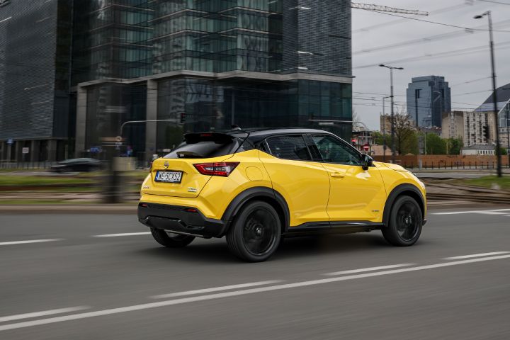 Jadący żółty Nissan Juke (widok z boku) z budynkami w tle