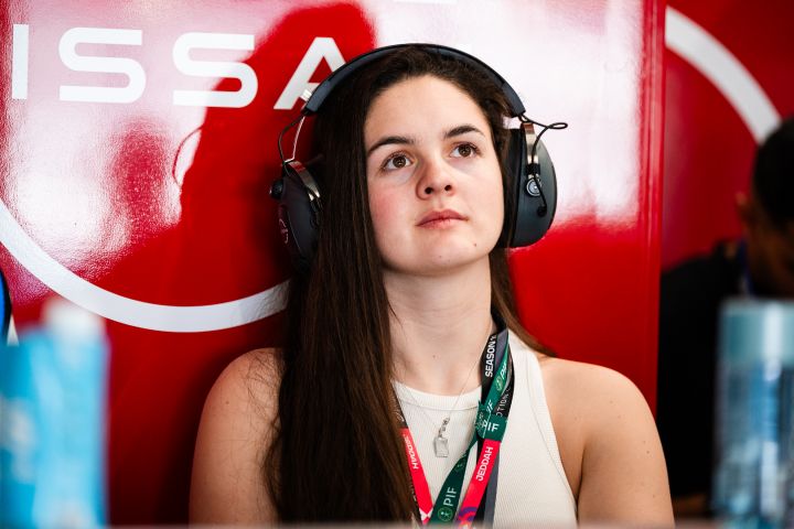 Abbi Pulling, Rookie und Simulator-Fahrerin des Nissan Formula E Teams, trägt Kopfhörer vor einem roten Hintergrund, hinter ihr ist teilweise das Nissan-Logo zu sehen.